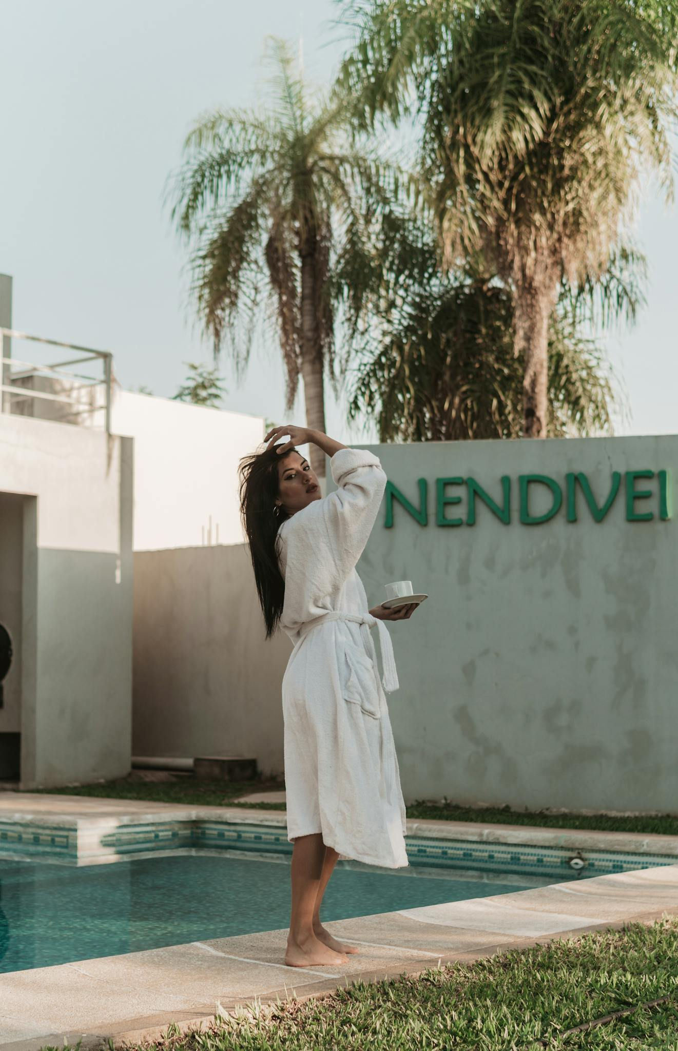 A serene outdoor scene featuring a woman in a bathrobe by a swimming pool, embracing a tranquil moment.