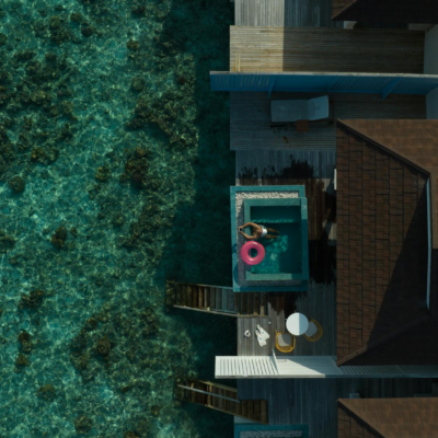 Stunning aerial view of a Maldives overwater villa with clear lagoon, featuring a bright pool float.