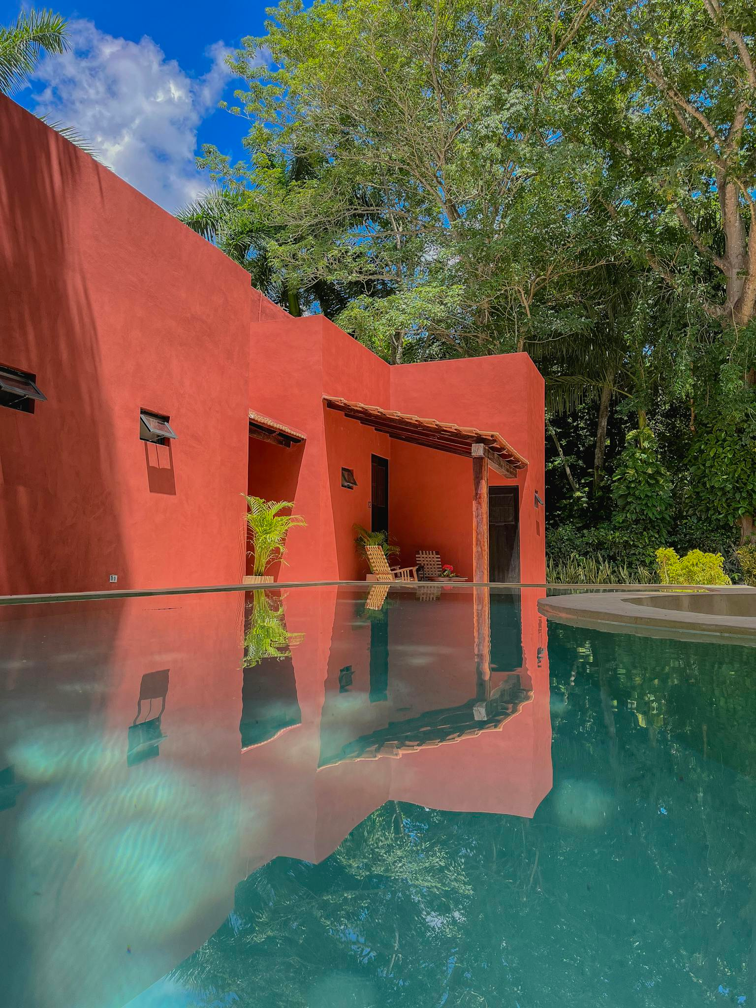 Vibrant red bungalow with pool reflection surrounded by lush greenery, ideal for travel inspiration.