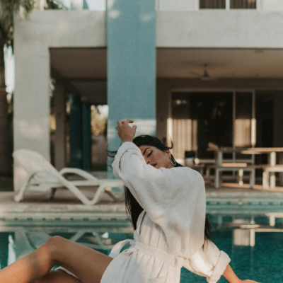 Woman in a bathrobe enjoying a sunny day by the pool at a modern villa.